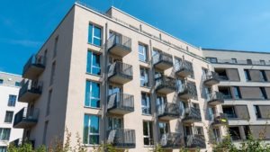Modern midrise apartment building with balconies and large windows, showcasing compact, daylight-rich housing design.